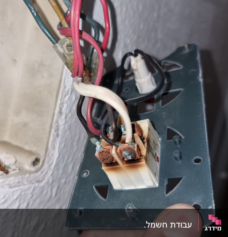 חוטי חשמל צבעוניים מחוברים לשקע חשמלי פתוח